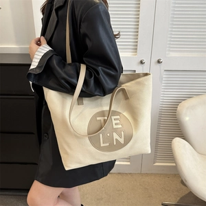 Detail of minimalist cream canvas tote bag with round leather patch and shoulder straps