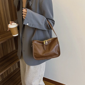 Detailed view of brown litchi pattern PU leather shoulder bag on model in a suit