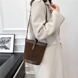 Detail of a luxury dark brown suede bucket bag featuring smooth leather trim and metal buckles