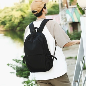 Rear view of a black minimalist nylon backpack worn by a man in an outdoor park setting