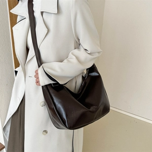 Detail shot of a dark brown large Hobo bag with glossy leather finish on a white trench coat