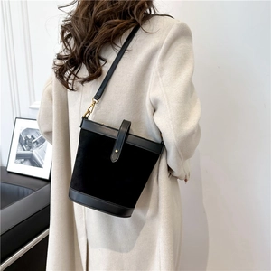 Elegant black suede bucket bag with adjustable leather strap shown on model's shoulder