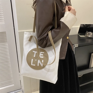 Detail of white canvas tote bag with round khaki leather patch and letter logo on front