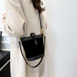 Detail of a black bucket bag with gold hardware worn by a model on the side