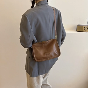 Detail of a brown PU leather crossbody bag with an embossed logo plate and adjustable strap