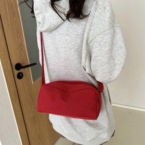 Minimalist red nylon crossbody shoulder bag for women worn by model in a casual indoor setting