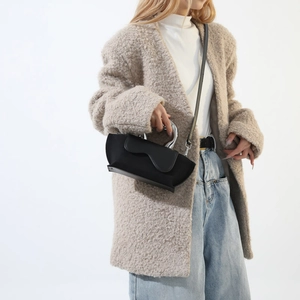 Detail view of black suede crossbody bag with silver metal handle on beige outfit