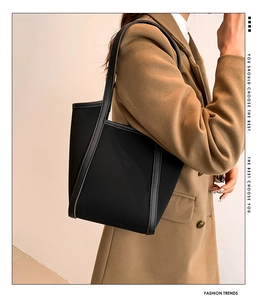 Detail of a black high-end PU tote bag styled with a brown wool suit and chic branding text