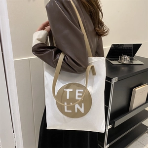 Detail of white canvas tote bag with brown leather straps and circular logo patch