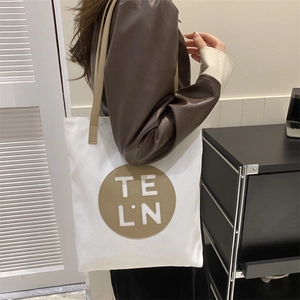 Detail of canvas shoulder bag with brown circular leather patch and TELN lettering
