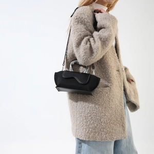 Detail of minimalist black PU handbag with wave flap and silver U-shaped metal handle
