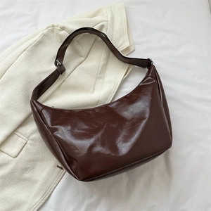 Detail of dark brown glossy PU leather hobo bag on beige blazer background