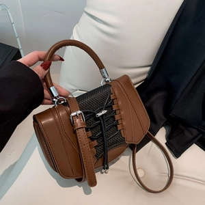 Detail of a brown leather saddle bag featuring a metal ring handle and woven lace decor