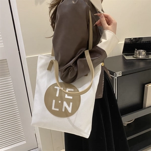 Detail shot of white canvas tote bag with brown leather patch and logo worn on shoulder