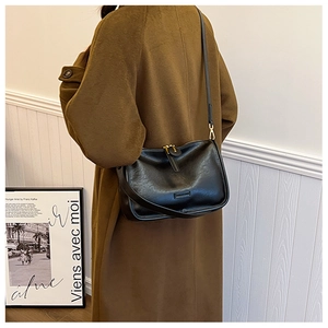 Detail of minimalist black PU leather crossbody bag worn over a dark brown winter wool coat