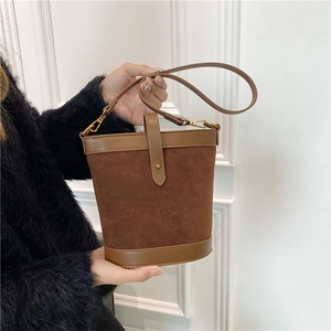 Close-up of brown suede bucket bag featuring leather trim and gold metal hardware hooks