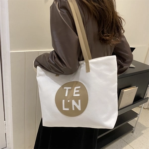 Detailed view of white canvas tote bag with brown leather logo patch and slim strap