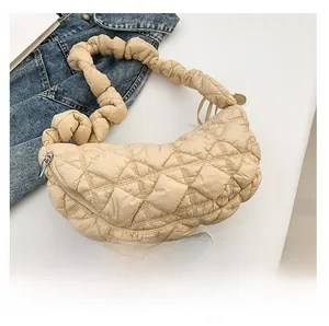 Detailed view of beige quilted cloud bag with ruched strap and metal zipper on white table