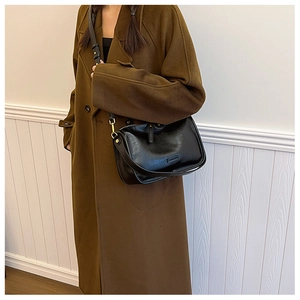 Detail view of the black PU leather crossbody bag worn by a model in a wool coat