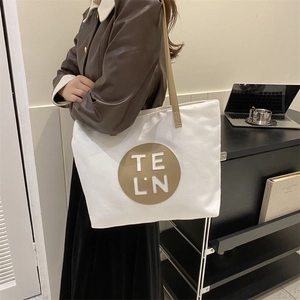 Minimalist canvas tote bag in off-white with brown leather strap and circular patch
