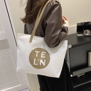 Detail of white canvas tote bag with brown leather patch and handle on a model