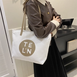 Close-up of beige canvas tote bag with brown leather details and TE L.N logo