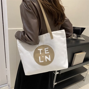 Close-up of minimalist canvas tote bag with leather logo patch and slim shoulder straps