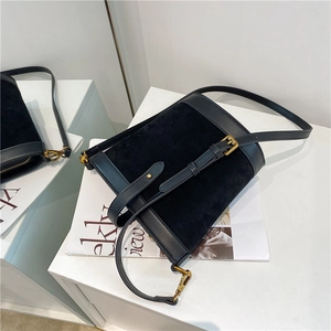 Detail view of black bucket bag showing suede and smooth leather texture with gold buckles