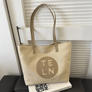 Detail of minimalist beige canvas tote bag with leather logo patch and long slim handles