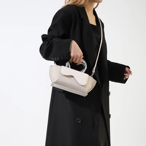 Minimalist beige handbag featuring a unique circular silver metal handle and smooth texture