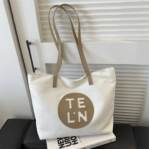 Detail of canvas tote bag with brown leather strap and embroidered TE L·N logo on the front