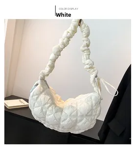 Detail of white quilted puffer bag featuring a crescent shape and ruched elastic shoulder strap