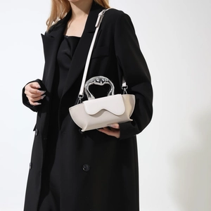 Detail of minimalist cream crescent bag with silver metallic handle on a black coat