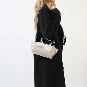 Detail of minimalist wave-pattern handbag with curved silver metal handle on black coat