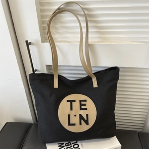 Detail of black canvas tote bag featuring khaki leather handles and circular logo patch