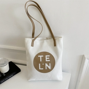 Detail of minimalist canvas tote bag with brown leather circular logo patch and strap
