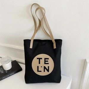 Detail of minimalist black canvas tote bag featuring beige round patch with TE L.N logo