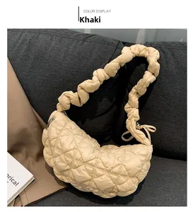 Detail view of khaki quilted puffer handbag with ruched handle on a grey sofa