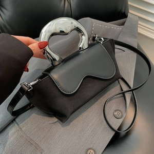 Detail of a black handbag with a wave-flap design and unique silver mirror handle