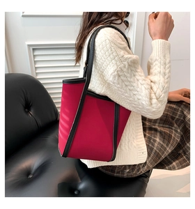 Detail view of red tote bag with black leather trim worn over the shoulder by a model