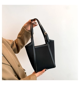 Close-up of black PU tote bag with leather straps and gold buckle on a camel coat