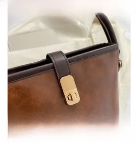 Nahaufnahme einer braunen Kunstledertasche mit goldenem Metall-Drehverschluss-Detail