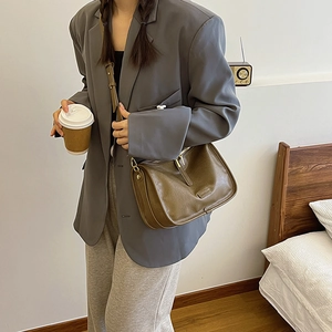Brown leather crossbody bag with metal zipper shown on model in a casual grey suit