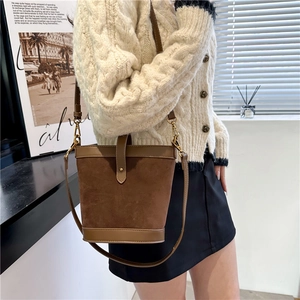 Brown suede and smooth leather bucket bag worn as a crossbody bag by a female model