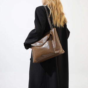 Détail du sac cabas en cuir PU marron avec chaîne argentée et fermoir sur un manteau noir