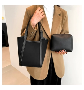 Close-up of minimalist black tote bag set with a matching pouch worn by a model in a blazer
