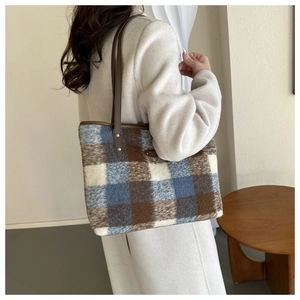 Detail of wool-blend tote bag showing brown and blue plaid texture with leather strap