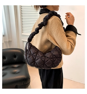 Detail showing black quilted crescent bag with ruffled strap worn by model in a modern room