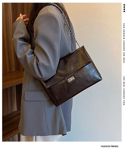 Close-up of a glossy black chain bag with silver buckle worn with a gray suit