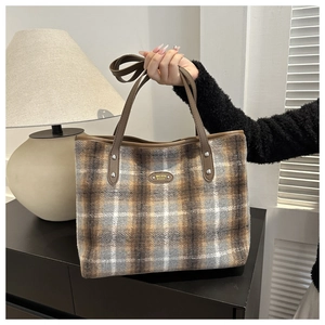 Detail of checkered tote bag with brown leather handles and golden metal logo